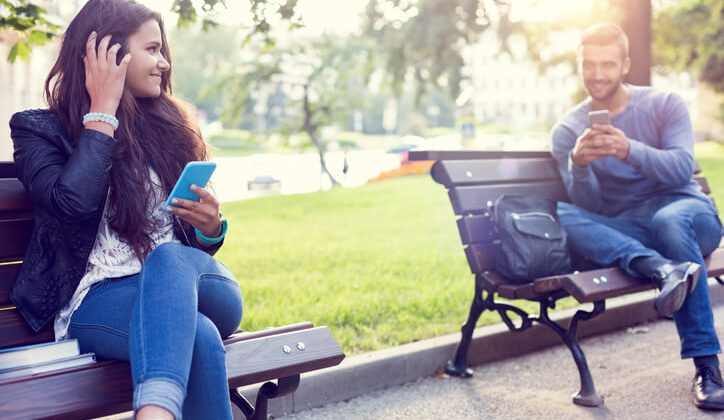 A Girl sitting in a park flirting over text with the boy sitting next to her