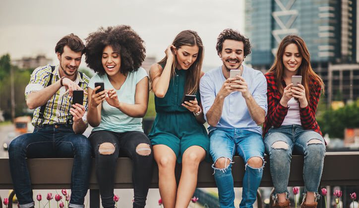 Friends sitting outdoor talking about trendy smartphones
