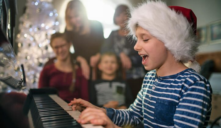 Little boy playing carols on piano on Christmas. Family has gathered near the Christmas tree. Nikon D850
