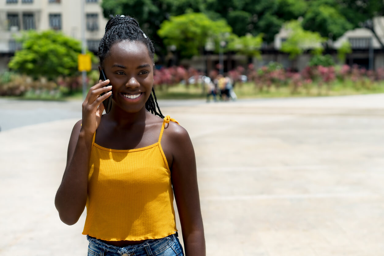 young adult calling nigeria and laughing at phone outdoor in summer in city